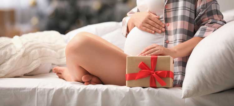 kobieta w ciąży siedząca na łóżku z prezentem w pudełku