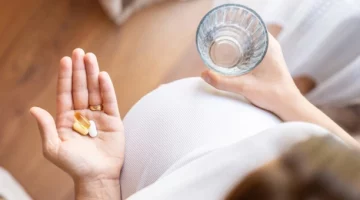 Kobieta w ciąży zażywająca paracetamol, popijając szklanką wody