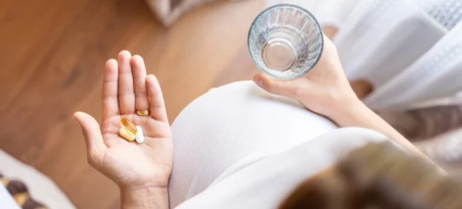 Kobieta w ciąży zażywająca paracetamol, popijając szklanką wody