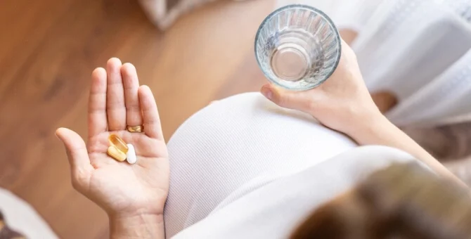 Kobieta w ciąży zażywająca paracetamol, popijając szklanką wody