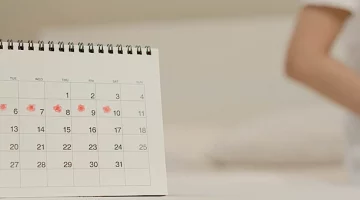 Kalendarz miesiączkowy, w tle siedząca kobieta