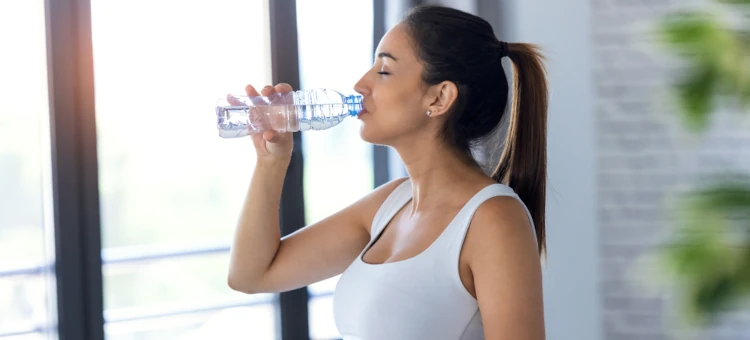 Kobieta w ciąży w białej koszulce pije wodę z butelki