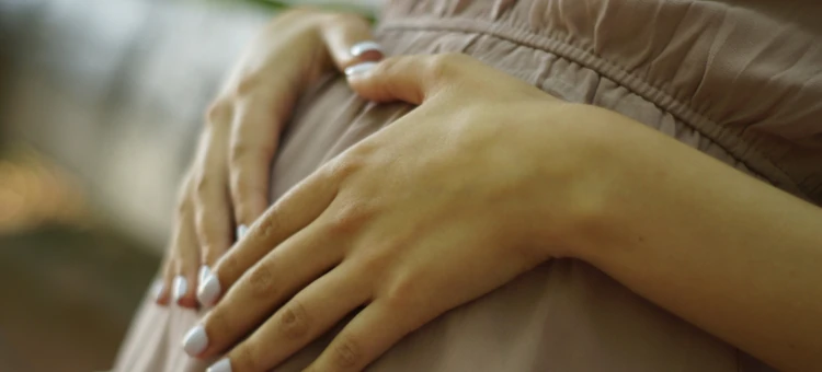 Kobieta w ciąży układa ręce na brzuchu