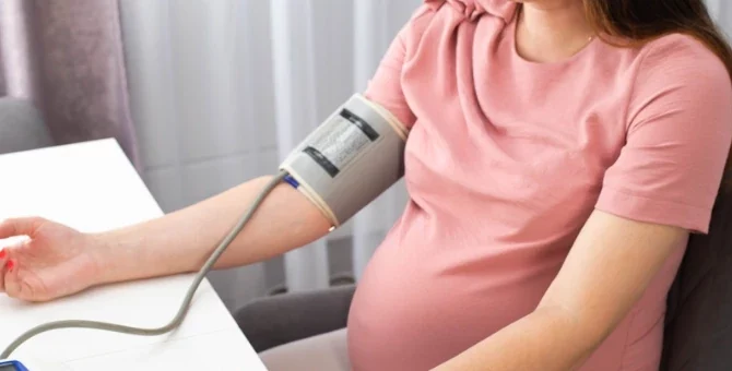Kobieta w ciąży mierzy ciśnienie z ręką na stole