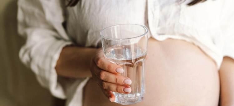 Kobieta w ciąży trzymająca szklankę wody – nawodnienie przy opuchniętych nogach i obrzękach w ciąży