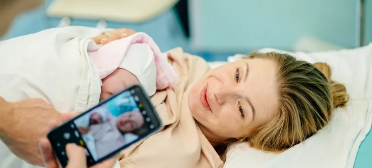 Szczęśliwa kobieta i ojciec wspierający ją po urodzeniu dziecka, robiący pierwsze zdjęcie swojego dziecka w sali porodowej
