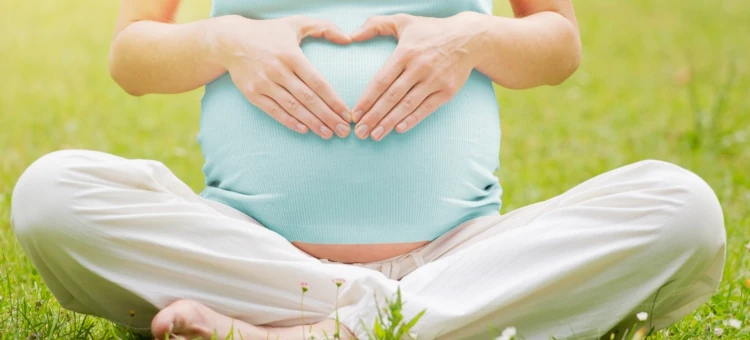 Kobieta w ciąży tworząca kształt serca na swoim brzuchu w świetle popołudniowego słońca