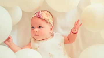 Portret małej, szczęśliwej dziewczynki otoczonej białymi balonami, symbolizującego radość z dzieciństwa i troskę o dziecko