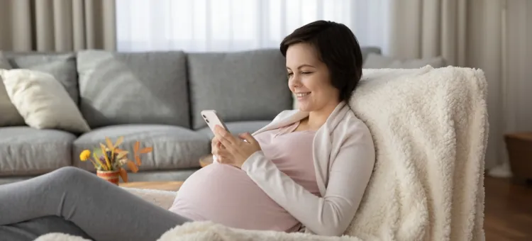 Młoda kobieta w ciąży korzysta z telefonu, sprawdza informacje o ciąży w internecie