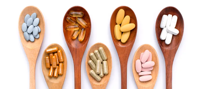 Różne rodzaje kapsułek z lekami i tabletek na drewnianych łyżkach, izolowane na białym tle. Zdrowe suplementy, zioła, witaminy i koncepcja diety.
