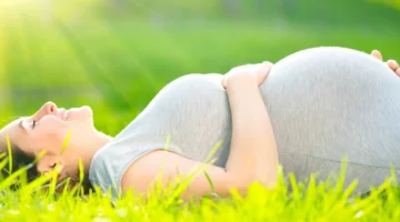 Szczęśliwa kobieta w ciąży dotyka swojego brzucha, leżąc na zielonej trawie i ciesząc się naturą