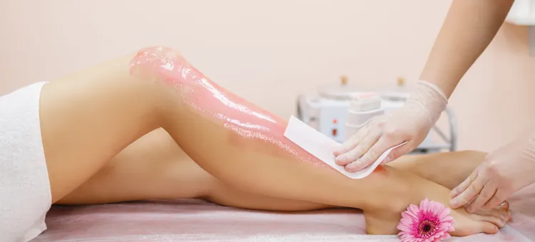 Kosmetyczka nakłada różowy wosk na nogę kobiety w celu depilacji