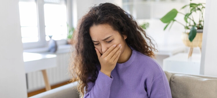 Kobieta siedząca na kanapie, trzymająca dłoń przy ustach z powodu nudności