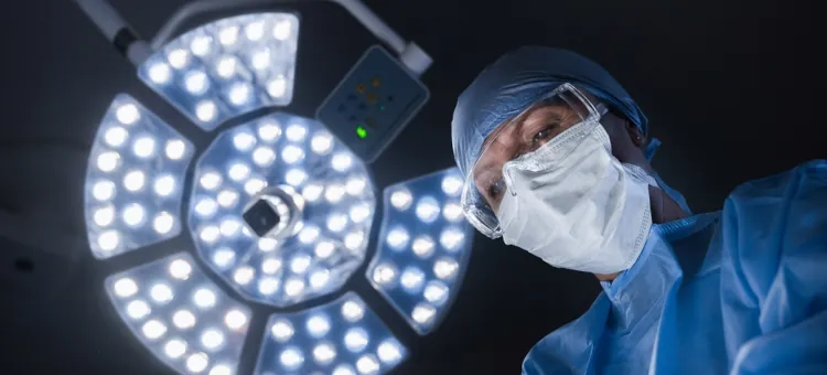 Lekarka koncentruje się, wykonując operację, w tle lampa chirurgiczna
