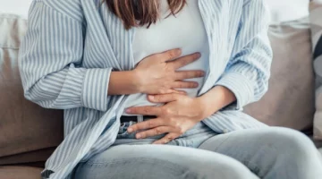 Kobieta siedząca na kanapie, trzymająca się za brzuch, mogąca odczuwać objawy sugerujące ciążę