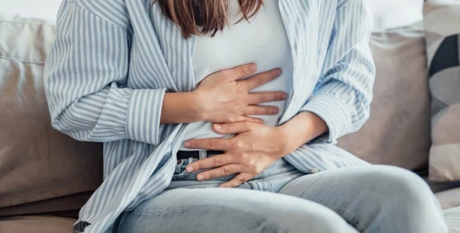 Kobieta siedząca na kanapie, trzymająca się za brzuch, mogąca odczuwać objawy sugerujące ciążę