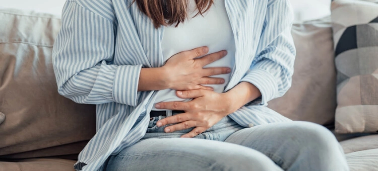 Kobieta siedząca na kanapie, trzymająca się za brzuch, mogąca odczuwać objawy sugerujące ciążę
