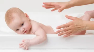 Ręce młodej matki próbują złapać niemowlę, leżące na białym materacu