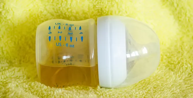 Pełna butelka herbaty z rumianku dla niemowlęcia, odwrócona na bok, na żółtym tle z materiału