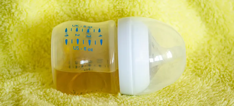 Pełna butelka herbaty z rumianku dla niemowlęcia, odwrócona na bok, na żółtym tle z materiału