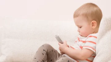 Mały chłopiec siedzi na kanapie w salonie podczas zabawy smartfonem, uczy się obsługi