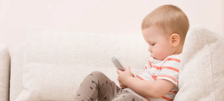 Mały chłopiec siedzi na kanapie w salonie podczas zabawy smartfonem, uczy się obsługi