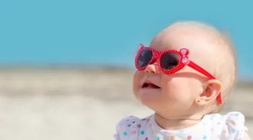 W słoneczny dzień mała dziewczynka siedzi na plaży i patrzy do góry