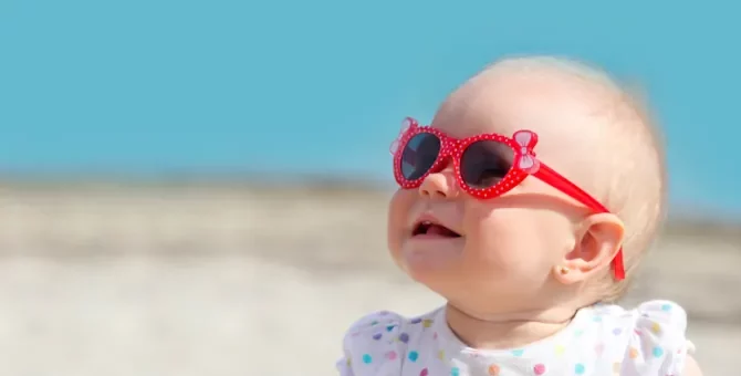 W słoneczny dzień mała dziewczynka siedzi na plaży i patrzy do góry