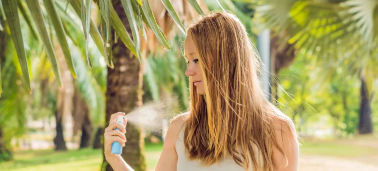 Kobieta w kraju tropikalnym aplikuje środek w postaci sprayu przeciw owadom na skórę