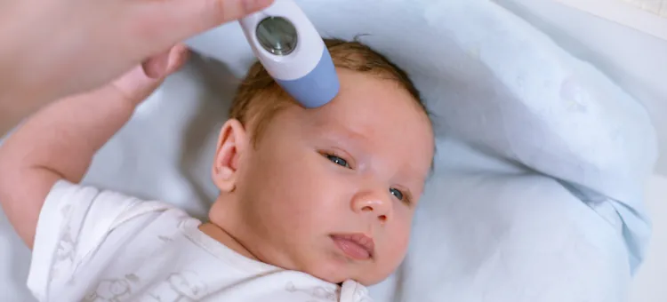 Mama mierzy temperaturę ciała noworodka za pomocą termometru bezdotykowego w pobliżu głowy dziecka