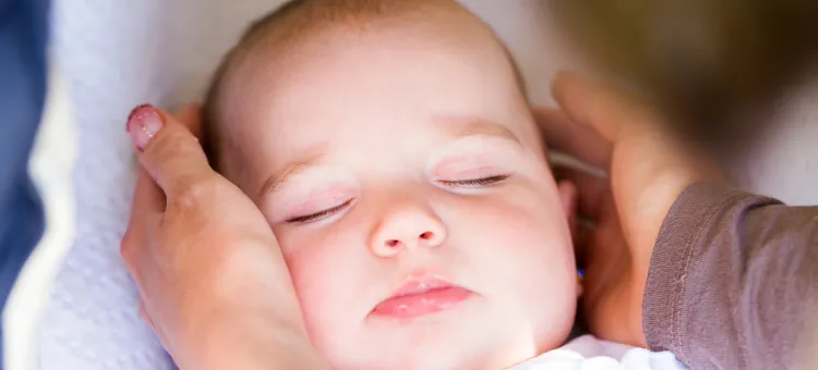 Zbliżenie śpiącego niemowlęcia, ręce kobiety dotykają główki z obu stron