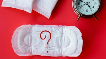 Spóźniający się okres – podpaska i budzik jako symbol opóźnienia miesiączki