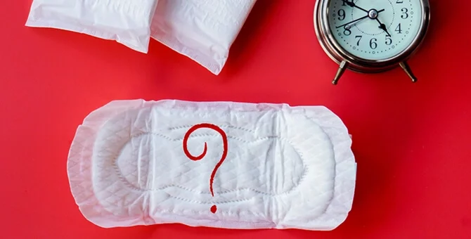 Spóźniający się okres – podpaska i budzik jako symbol opóźnienia miesiączki