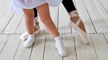 Tancerka baletowa i dziewczynka wykonują pozycję baletową na drewnianej podłodze, zbliżenie na układ nóg