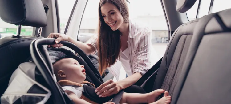 Uśmiechnięta mama z maluchem otworzyła drzwi samochodu i sprawdza bezpieczeństwo dziecka w foteliku bezpieczeństwa