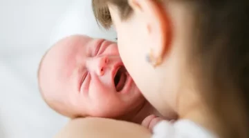 W objęciach matki płacze mały chłopiec, widać twarz dziecka i bok głowy matki