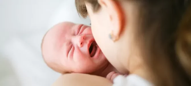 W objęciach matki płacze mały chłopiec, widać twarz dziecka i bok głowy matki