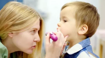 Badanie gardła małego chłopca podczas wizyty przez lekarkę, oświetlającą gardło dziecka