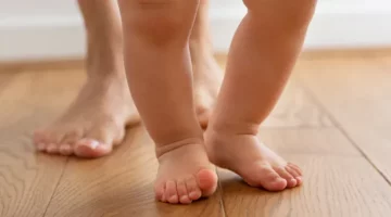 Drewniana podłoga z widocznymi stopami dorosłego i małego dziecka, które stawia kroki