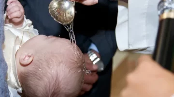 Podczas chrztu świętego duchowny polewa główkę dziecka wodą święconą