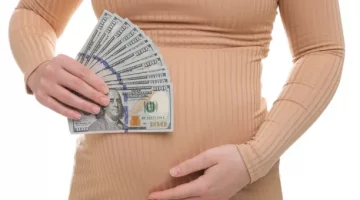 Ciężarna kobieta trzyma w dłoniach wachlarz dolarów