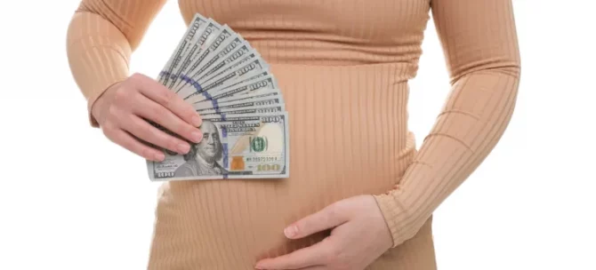 Ciężarna kobieta trzyma w dłoniach wachlarz dolarów