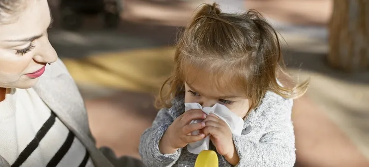 Dziewczynka z katarem wyciera nos chusteczką, obok mama