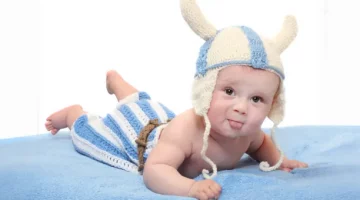 Urocze niemowlę w zabawnym stroju wikinga leży na brzuchu na niebieskim kocyku