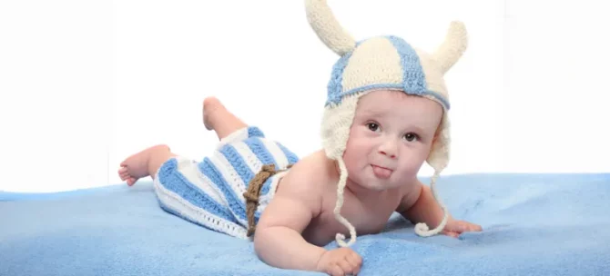 Urocze niemowlę w zabawnym stroju wikinga leży na brzuchu na niebieskim kocyku