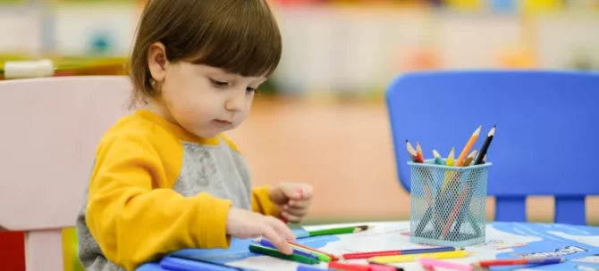 Dziewczynka dotyka kredek podczas rysowania obrazka leżącego na stoliku