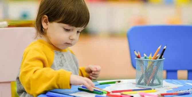 Dziewczynka dotyka kredek podczas rysowania obrazka leżącego na stoliku