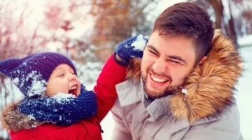 Uśmiechające się dziecko dotyka śnieżką twarzy śmiejącego się mężczyzny