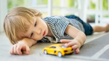 Chłopiec leżący na podłodze obok żółtego samochodzika, bawi się nim