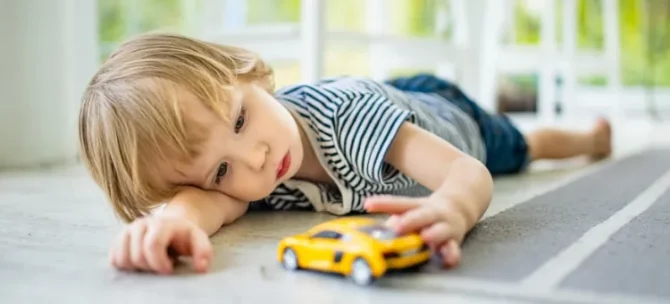Chłopiec leżący na podłodze obok żółtego samochodzika, bawi się nim